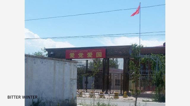 Die einzige Moschee, die im Viertel Bashiyu von Wusu übrig ist. Die Quertafel am Haupttor lautet: "Liebe die Partei, liebe dein Land." Man kann die chinesische Flagge und eine Überwachungskamera sehen.