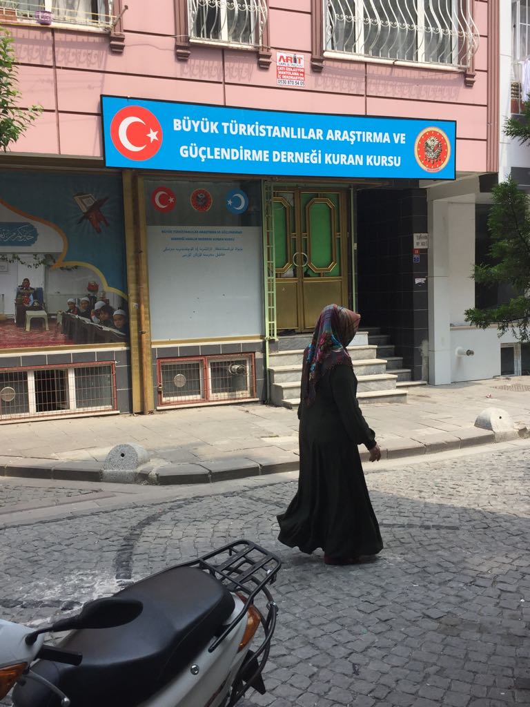 Eine Uigurenfrau geht an einer kleinen Medresse vorbei