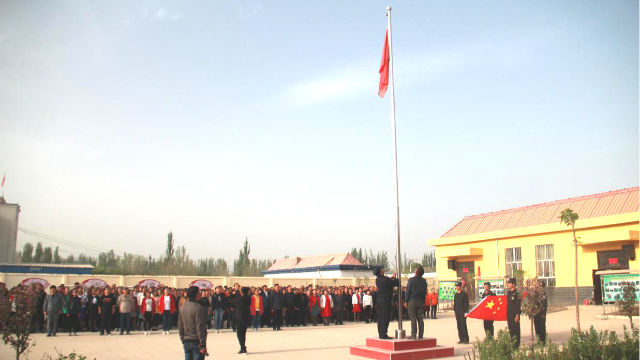 Die Menschen in einem Ort in Xinjiang sind organisiert, um eine Fahnenhebezeremonie abzuhalten
