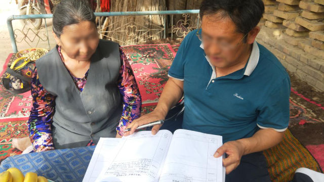 Regierungsbeamter in Xinjiang bittet eine ältere Frau, die Materialien zu lesen