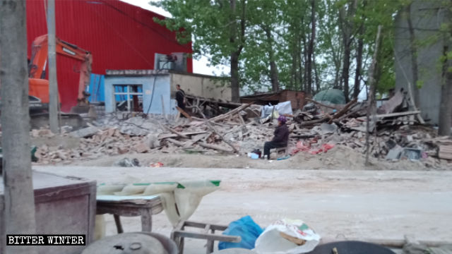 Ältere Frau sitzt neben den Ruinen ihres zerstörten Hauses